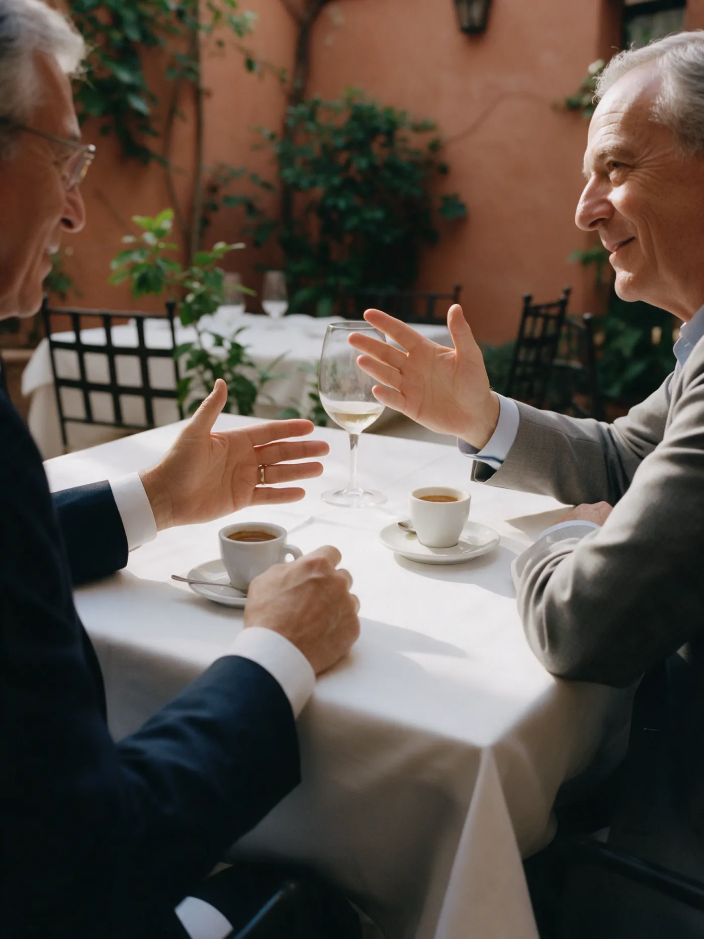 Two executives in conversation over coffee after lunch in a Madrid courtyard
